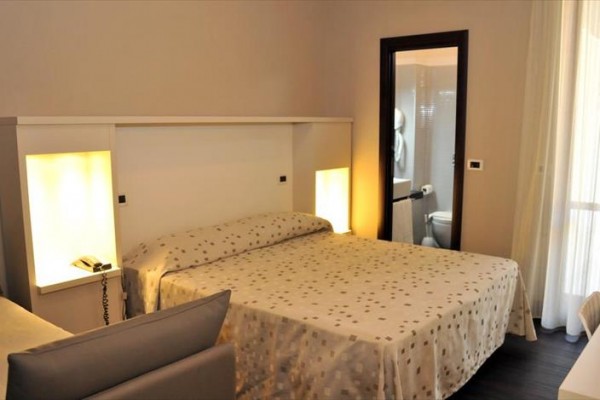 Nowoczesny pokój hotelowy z łóżkiem małżeńskim i widokiem na łazienkę z drzwiami.