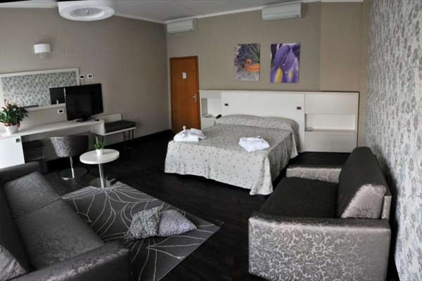Pokój hotelowy z podwójnym łóżkiem, sofą, telewizorem i dekoracją w neutralnych kolorach.