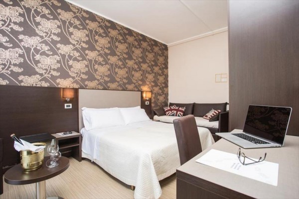 Elegancki pokój hotelowy z łóżkiem małżeńskim, sofą i biurkiem z laptopem.