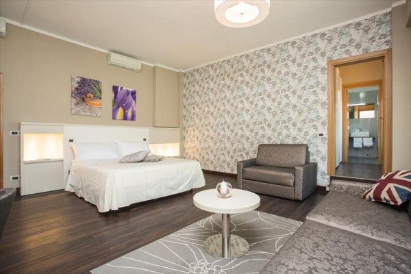 Nowocześnie urządzony pokój hotelowy z łóżkiem małżeńskim, sofami i łazienką.