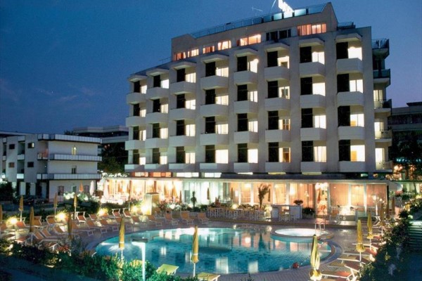 Hotel z oświetlonymi oknami i zewnętrznym basenem wieczorem.