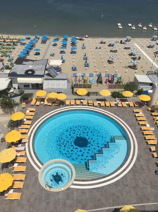 Okrągły basen z jacuzzi otoczony żółtymi leżakami i parasolami blisko plaży.  