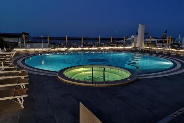 Zewnętrzny basen i jacuzzi oświetlone wieczorem z leżakami wokół.