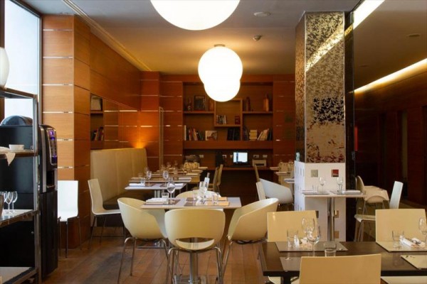 Nowoczesna restauracja z drewnianymi ścianami, półkami z książkami i okrągłymi wiszącymi lampami.