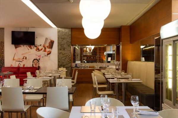 Nowoczesna restauracja z białymi stołami, czerwoną kanapą i dekoracjami na ścianach.