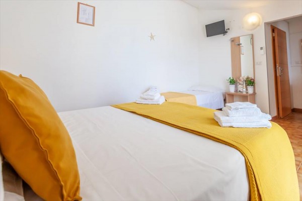 Jasny pokój hotelowy z łóżkiem, żółtymi dodatkami i telewizorem na ścianie.