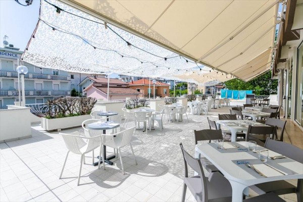 Taras restauracji z białymi stołami i krzesłami pod markizami.