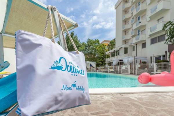 Torba plażowa wisząca na leżaku przy basenie, w tle budynek hotelowy.