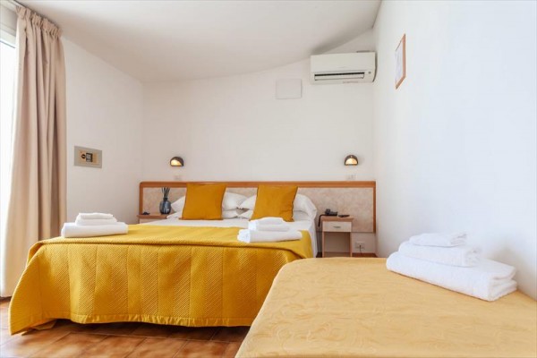 Prosto urządzony pokój hotelowy z dwoma łóżkami i żółtą pościelą.