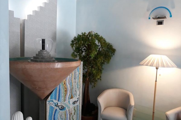 Wnętrze z dekoracyjną fontanną, rośliną, fotelami i lampą.