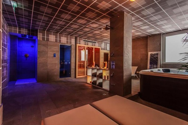 Pomieszczenie wellness z jacuzzi, prysznicem i sauną, o stonowanym oświetleniu.