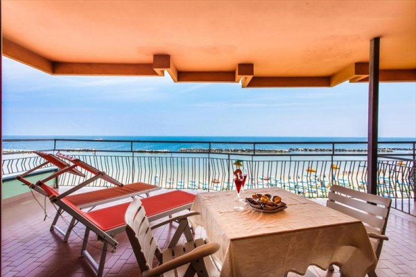 Balkon z widokiem na plażę i morze, stolik i leżaki.