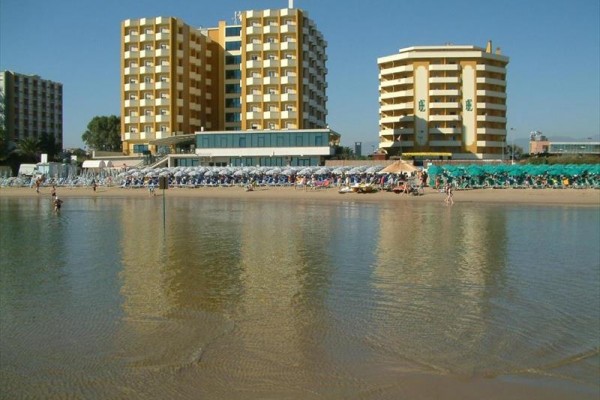 Piaszczysta plaża z leżakami i kilkoma wysokimi budynkami w tle.