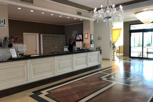 Recepcja hotelowa z żyrandolem, ladą i recepcjonistką za biurkiem.
