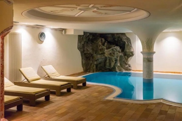 Kryty basen z leżakami i sztuczną dekoracją skalną.
