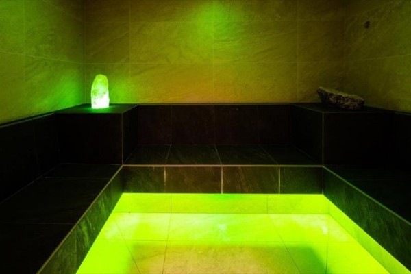 Sauna parowa z czarnymi ławkami i zielonym oświetleniem.