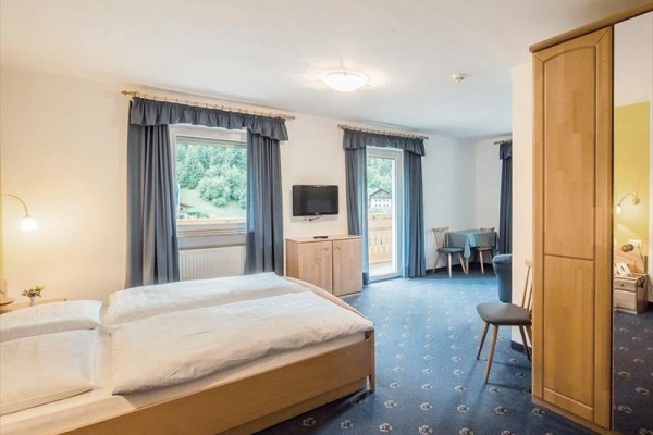 Jasny pokój z podwójnym łóżkiem, telewizorem i balkonem, z widokiem na zielony krajobraz.