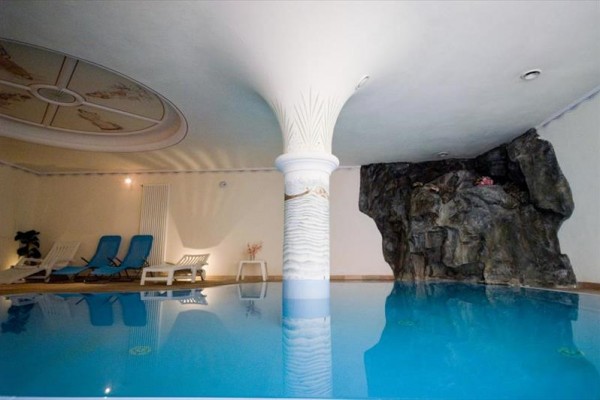 Basen kryty z leżakami i ozdobną skałą.