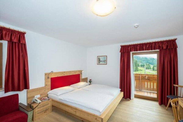 Pokój z drewnianym łóżkiem, czerwonymi zasłonami i balkonem z widokiem na krajobraz.