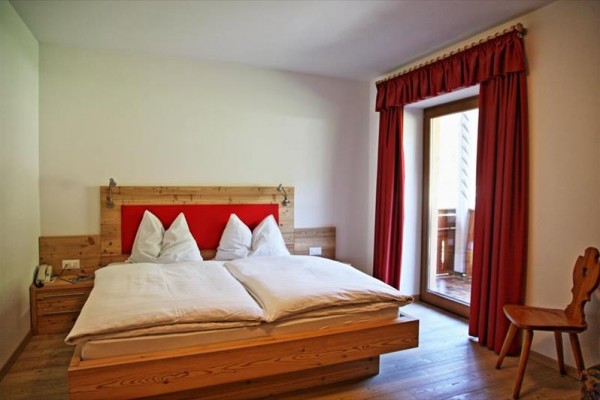 Łóżko dwuosobowe w pokoju hotelowym z czerwonymi zasłonami przy balkonie.