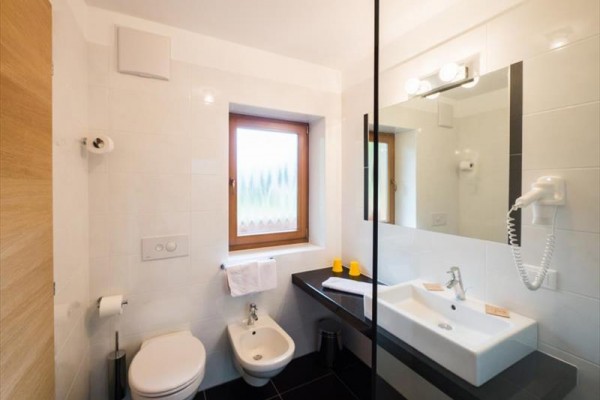 Łazienka z toaletą, bidetem, umywalką i lustrem obok okna.