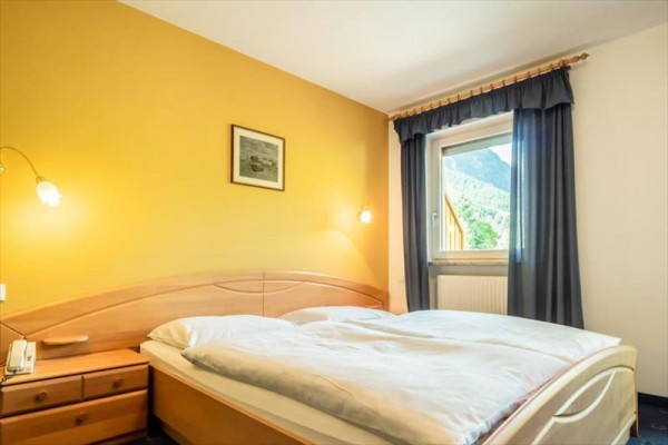 Pokój z łóżkiem małżeńskim, żółtą ścianą i oknem z widokiem na góry.