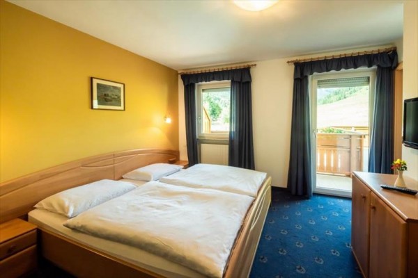 Pokój z dużym łóżkiem, żółtą ścianą i balkonem z widokiem na naturę.