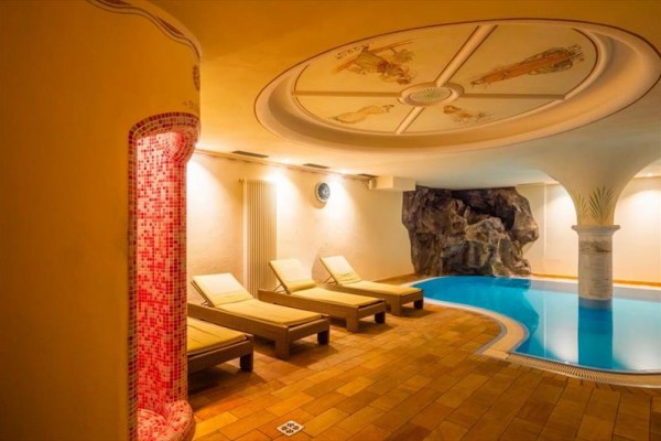 Strefa relaksu z leżankami i basenem we wnętrzu z ozdobnym sufitem.