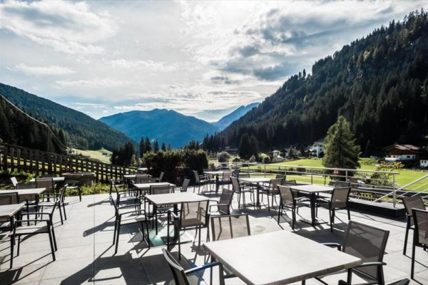 Górski taras z pustymi stolikami i krzesłami z widokiem na lasy i dolinę.