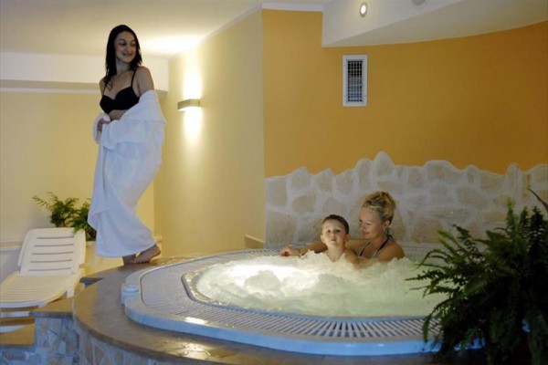 Kobieta stoi obok jacuzzi, w której siedzi inna kobieta z dzieckiem.
