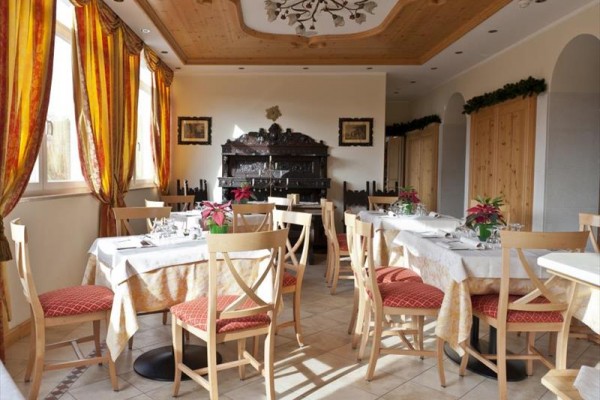 Restauracja z drewnianymi krzesłami i obrusami na stołach, ozdobiona świątecznymi roślinami.