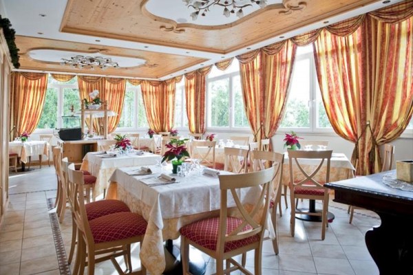 Przestronna restauracja z eleganckim drewnianym sufitem i czerwono-żółtymi zasłonami.