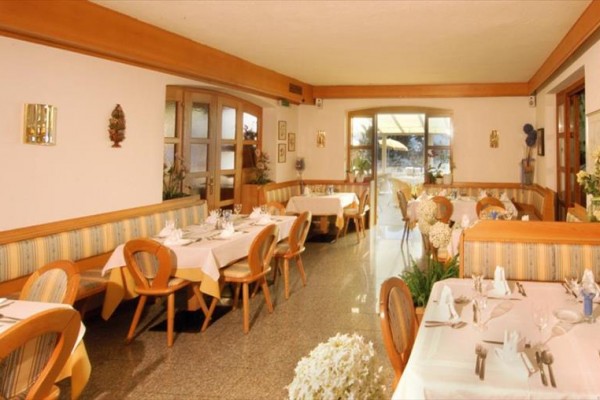 Wnętrze restauracji z drewnianymi krzesłami i stołami nakrytymi białymi obrusami.