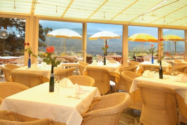 Elegancka restauracja z wiklinowymi meblami i widokiem na góry przez duże okna.