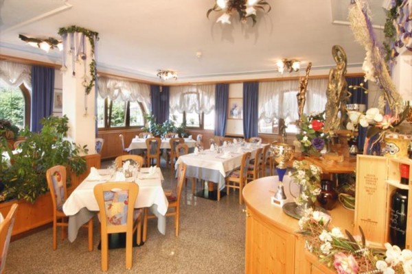 Restauracja z drewnianymi stołami, krzesłami i dekoracjami, z obrusami i kwiatami.