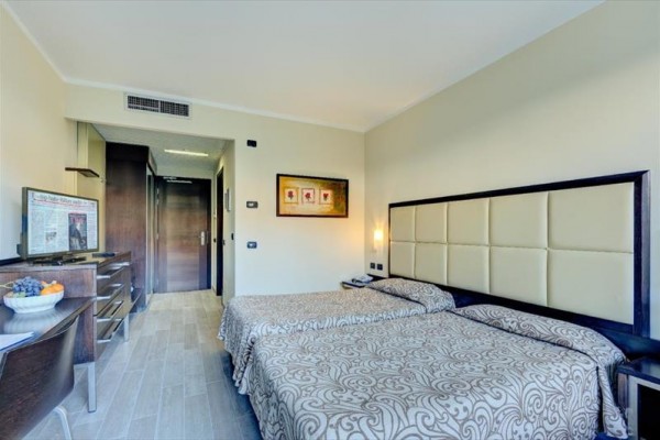 Dwa pojedyncze łóżka w jasnym pokoju hotelowym z nowoczesnymi meblami.