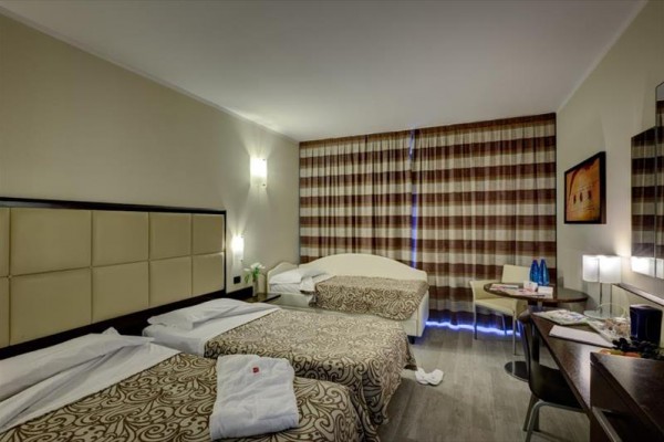 Pokój hotelowy z dwoma łóżkami, stołem i zasłonami na oknach.