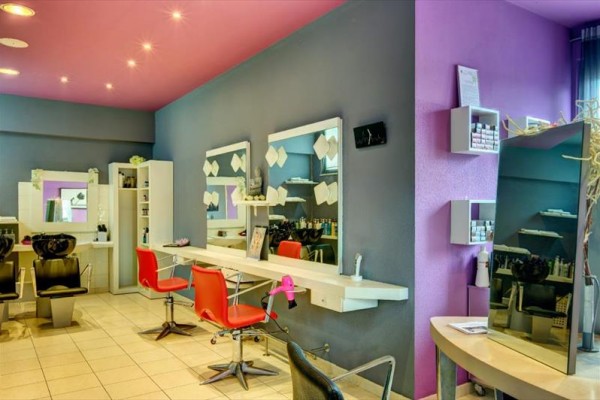 Wnętrze salonu fryzjerskiego z fioletowymi i szarymi ścianami, czerwonymi krzesłami i lustrami.