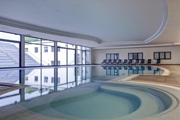 Kryty basen z jacuzzi i rzędem pustych leżaków przy ścianie.