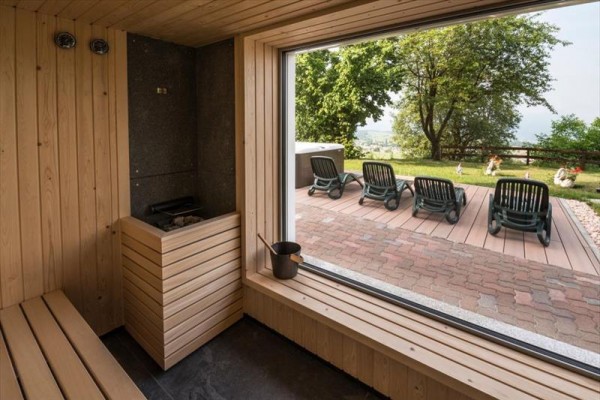 Widok z sauny na zewnętrzny taras z leżakami i ogrodem.