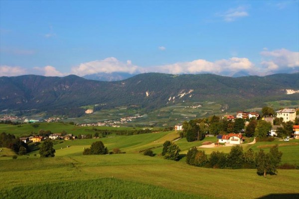 Wieś otoczona zielonymi łąkami i lasami z górskim pasmem w tle.