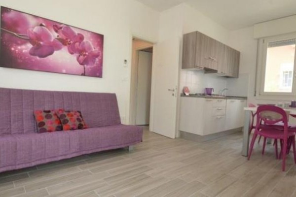 Nowoczesny salon z fioletową sofą, aneksem kuchennym i stołem jadalnym.
