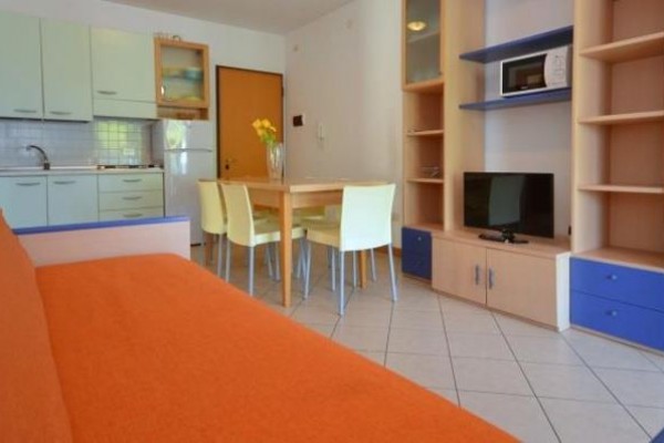 Salon z pomarańczową kanapą, aneksem kuchennym i stołem jadalnym.