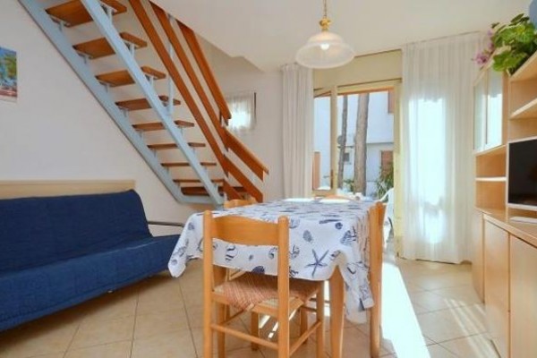 Salon z niebieską kanapą, drewnianymi schodami i stołem z obrusem w marynistyczny wzór.