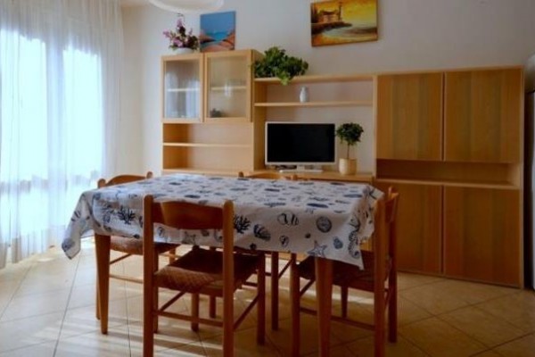 Jadalnia ze stołem, krzesłami, szafkami i telewizorem, oświetlona światłem dziennym z okna.