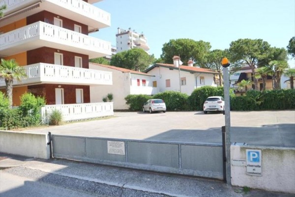 Brama garażowa przy bloku mieszkalnym z parkingiem i zaparkowanymi samochodami.