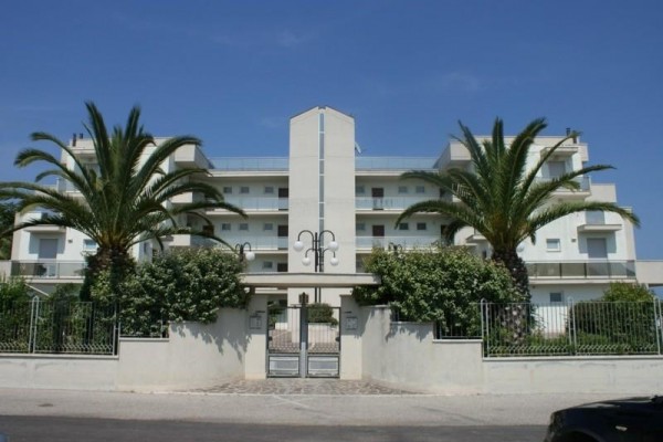 Nowoczesny wielopiętrowy budynek z dwoma palmami przy wejściu.