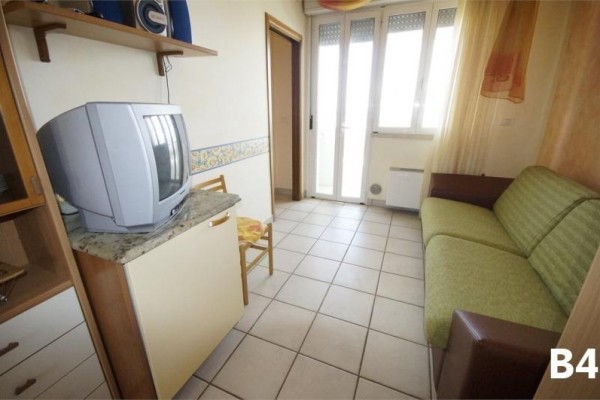 Mały pokój z kanapą, telewizorem i drzwiami balkonowymi.