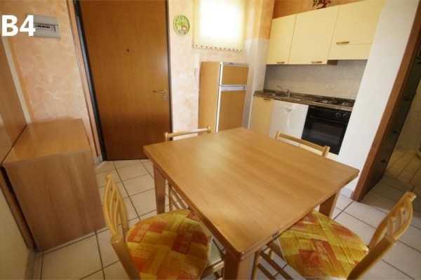 Kącik kuchenny z drewnianym stołem i czterema krzesłami, za nimi szafka kuchenna i sprzęty AGD.