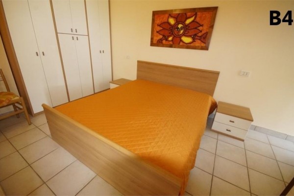 Sypialnia z dwuosobowym łóżkiem, pomarańczową narzutą i obrazem słońca nad łóżkiem.